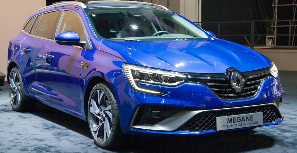 Couple avec leur fille inspectant le coffre ouvert d'une Renault Mégane Estate grise d'occasion sur un parking extérieur en fin d'après-midi