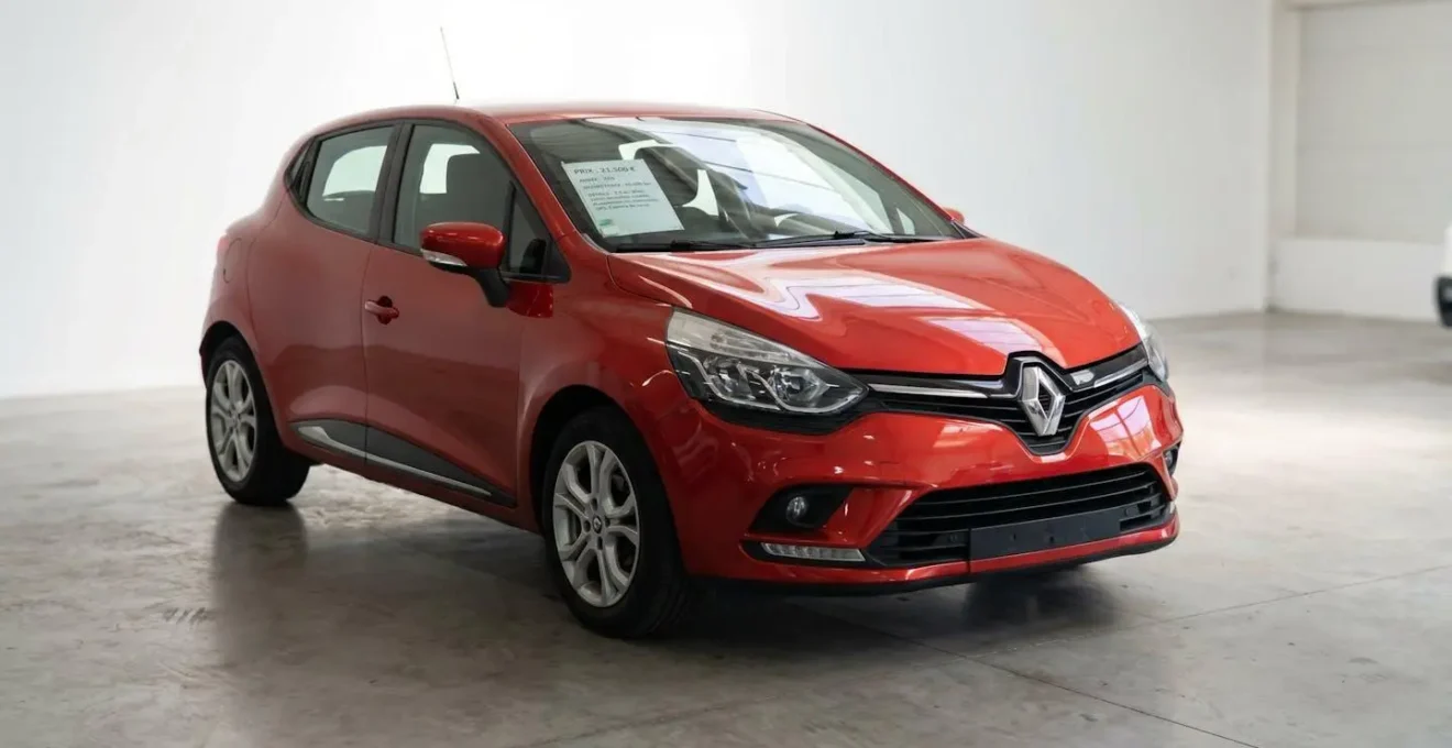 Renault Clio 4 rouge d'occasion en vue trois-quarts avant dans un showroom lumineux, avec étiquette de prix en français affichée sur la vitre latérale