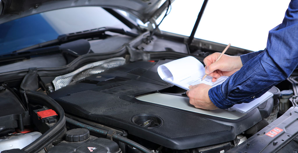 Mécanicien professionnel inspectant le moteur d'un véhicule Renault avec lampe LED, carnet d'entretien Renault ouvert posé sur l'aile avant du véhicule
